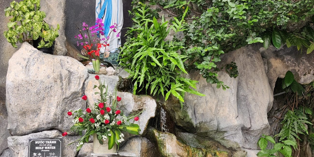 Grota z figurą matki bożej w da nang cathedral, otoczona kwiatami i zielenią.