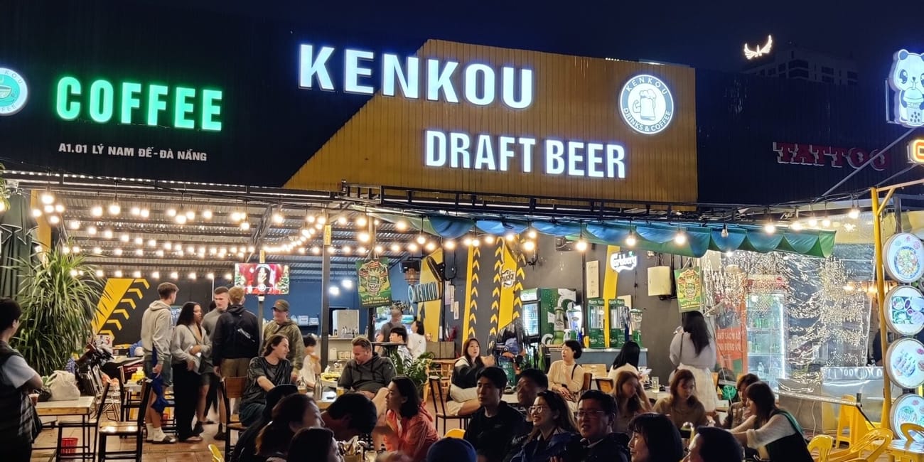 Wieczorny ogródek kenkou draft beer w da nang z grupami ludzi przy stolikach.