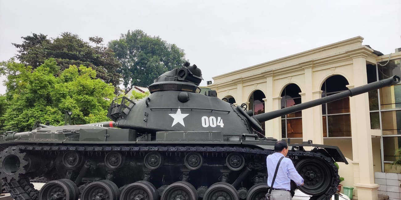 Czołg-pomnik przy hanoi flagtower z numerem 004 i białą gwiazdą, obok stoi mężczyzna.