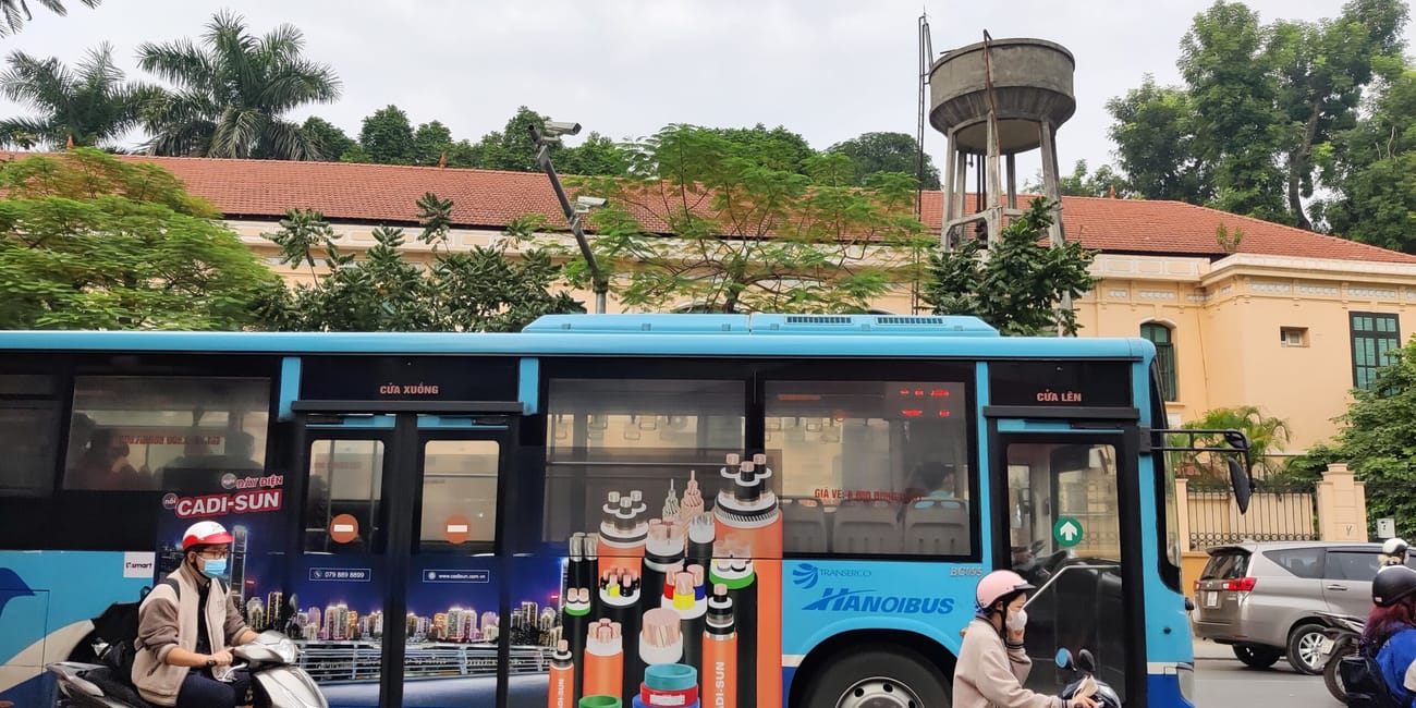 Autobus hanoibus i skutery na ulicy w hanoi, z budynkiem i wieżą wodną w tle