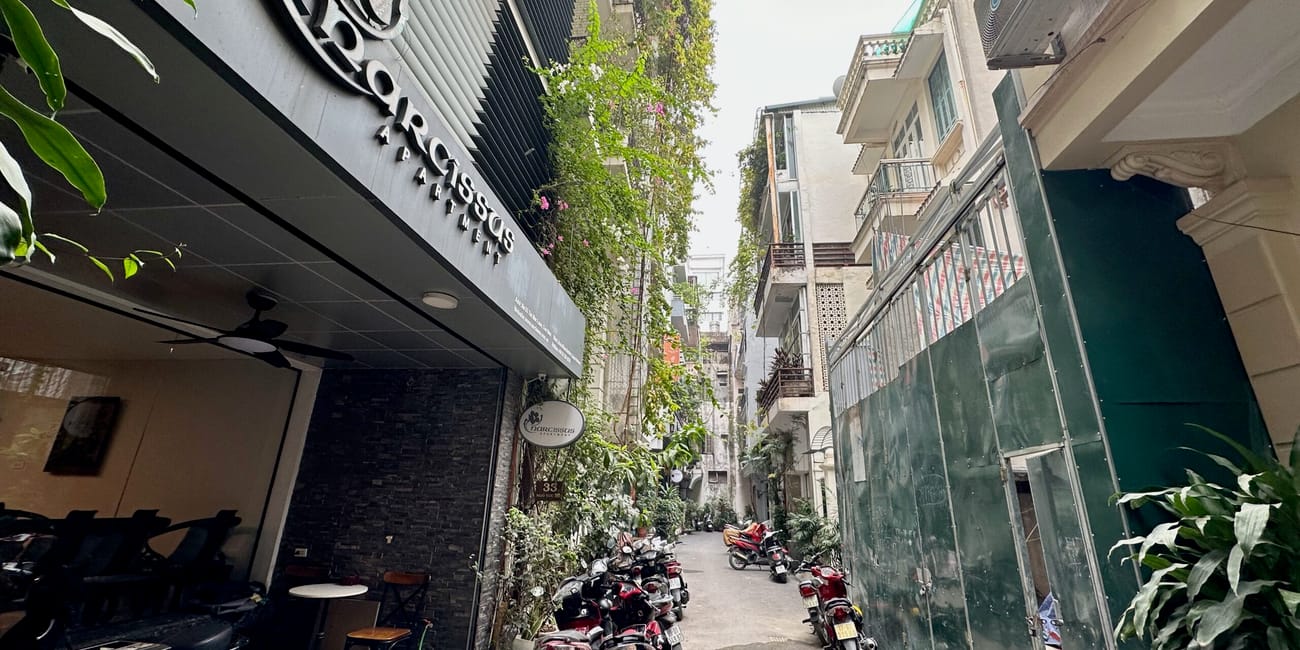Wąska uliczka w hanoi z zaparkowanymi skuterami i kawiarnią maison marou chocolatier.