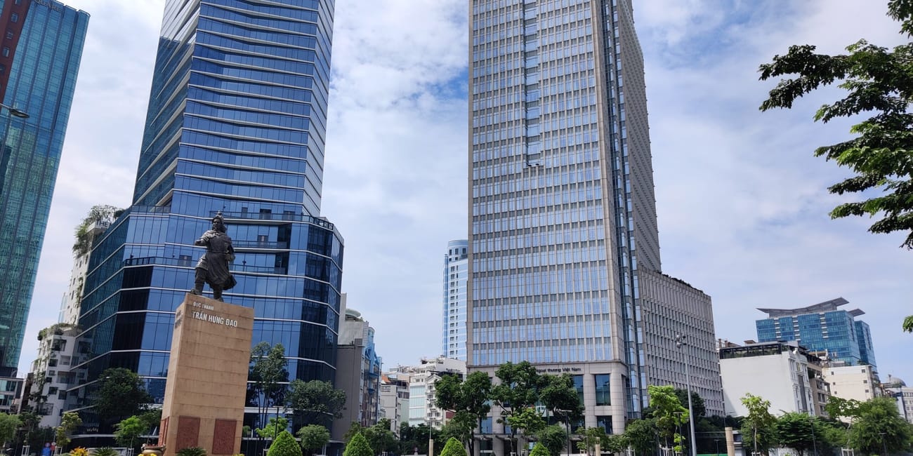 Pomnik trần hưng đạo w ho chi minh, otoczony wieżowcami przy ruchliwej ulicy.