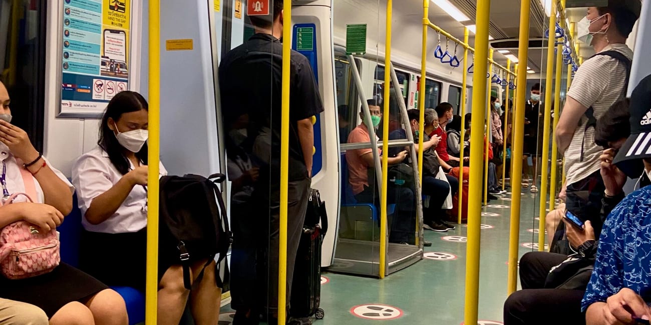 Wnętrze pociągu metra w bangkoku z pasażerami siedzącymi i stojącymi.
