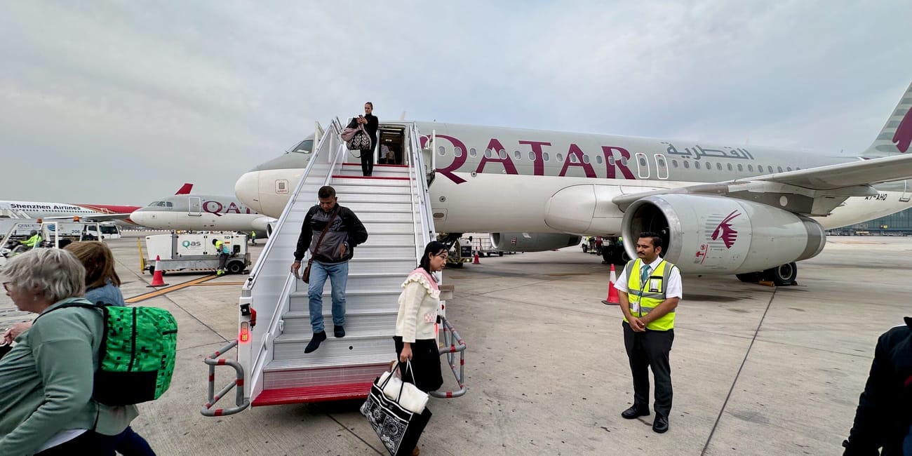 Pasażerowie schodzą po trapie z samolotu qatar airways na płycie lotniska w dosze.