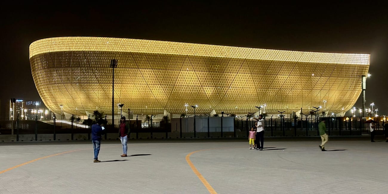Złocisty stadion w doha nocą, z kilkoma ludźmi na placu przed nim