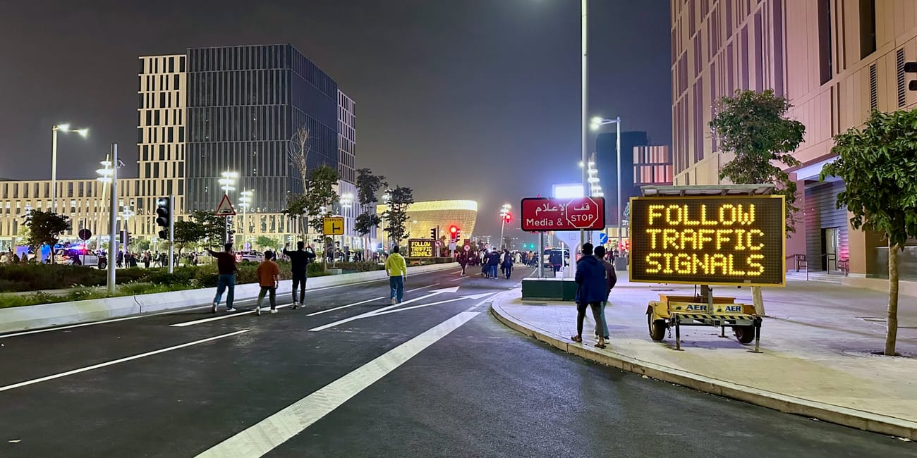 Nocna ulica w doha z ludziami, wieżowcami i tablicą „follow traffic signals”