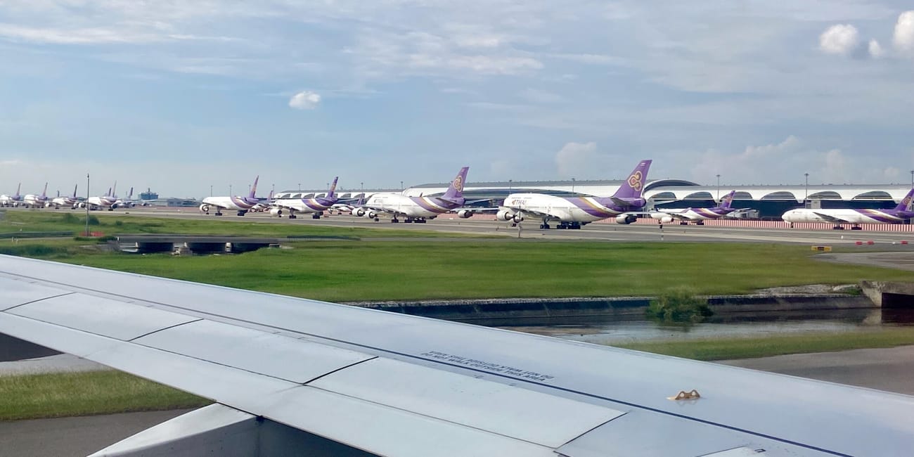 Skrzydło samolotu na lotnisku w bangkoku, w tle rząd samolotów thai airways.