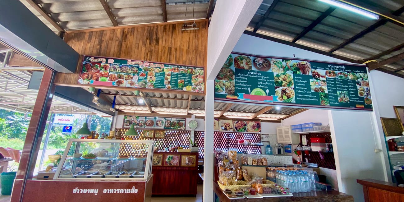 Wnętrze tajskiej restauracji w bangkoku z ladą, menu i wystawionymi potrawami.