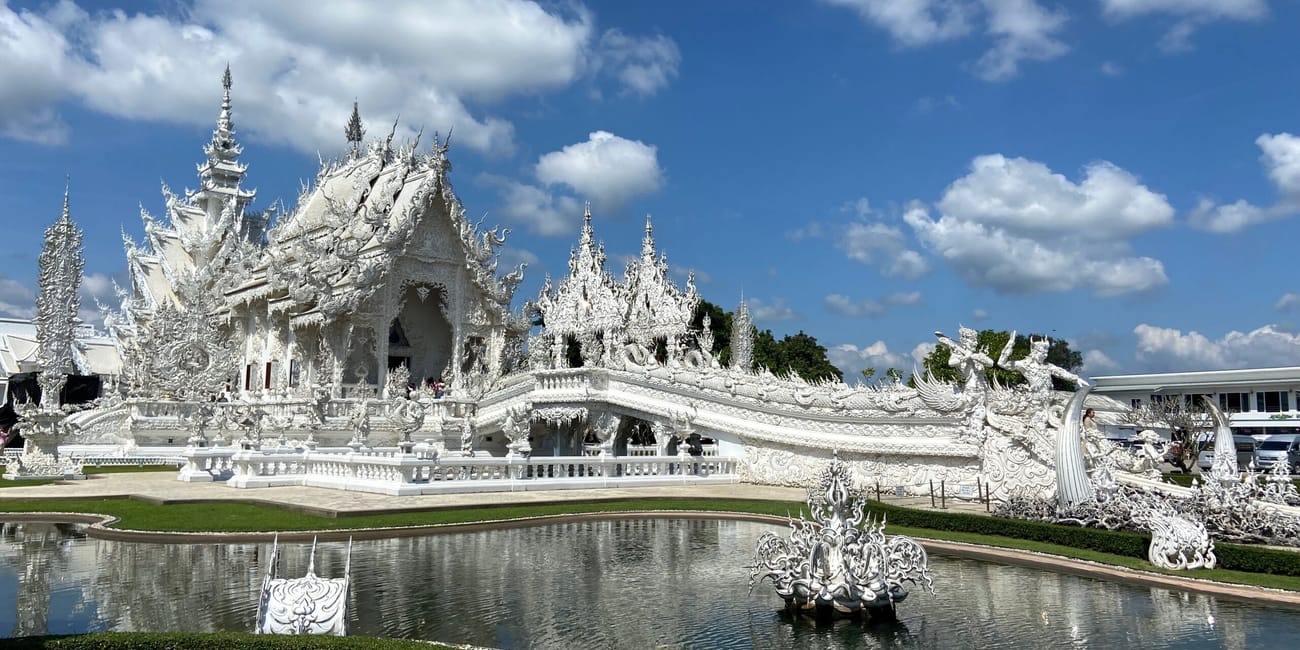 Biała świątynia wat rong khun w chiang rai, odbijająca się w stawie pod błękitnym niebem.