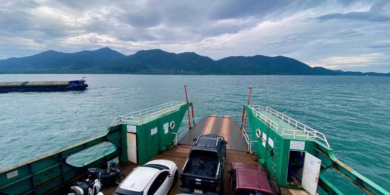 Prom na koh chang z samochodami i skuterami, na tle gór i morza pod pochmurnym niebem