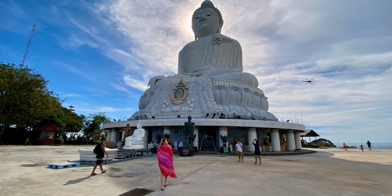 Wielki posąg buddy w phuket big buddha na wzgórzu, z kilkoma turystami na placu.