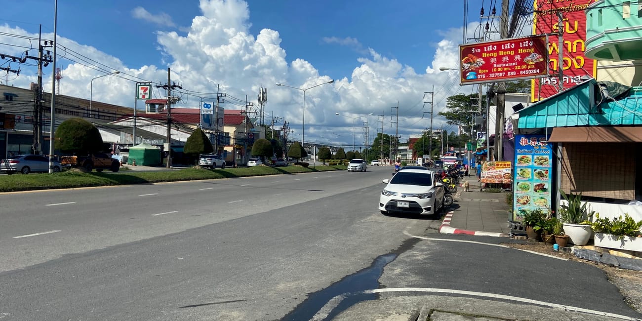 Ulica w phuket w tajlandii z ruchem samochodowym, sklepami i wysokimi chmurami na niebie