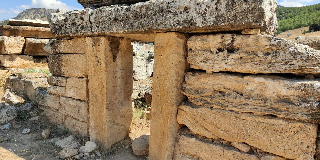 Grobowiec w nekropolii hierapolis w pamukkale, z kamiennym wejściem i ruinami na tle nieba.