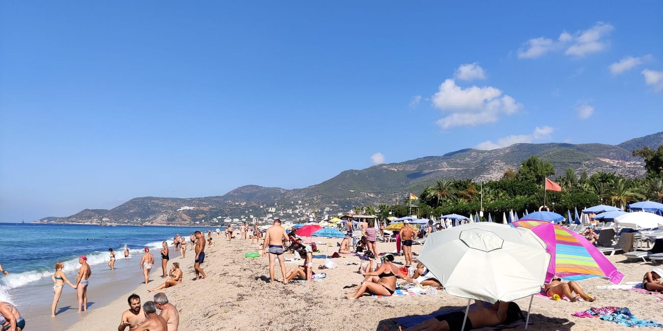 Plaża kleopatra na tureckiej riwierze z plażowiczami, parasolami i górami w tle