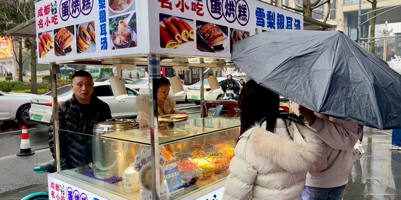 Stoisko z przekąskami w chengdu, z ludźmi stojącymi w kolejce pod parasolem.