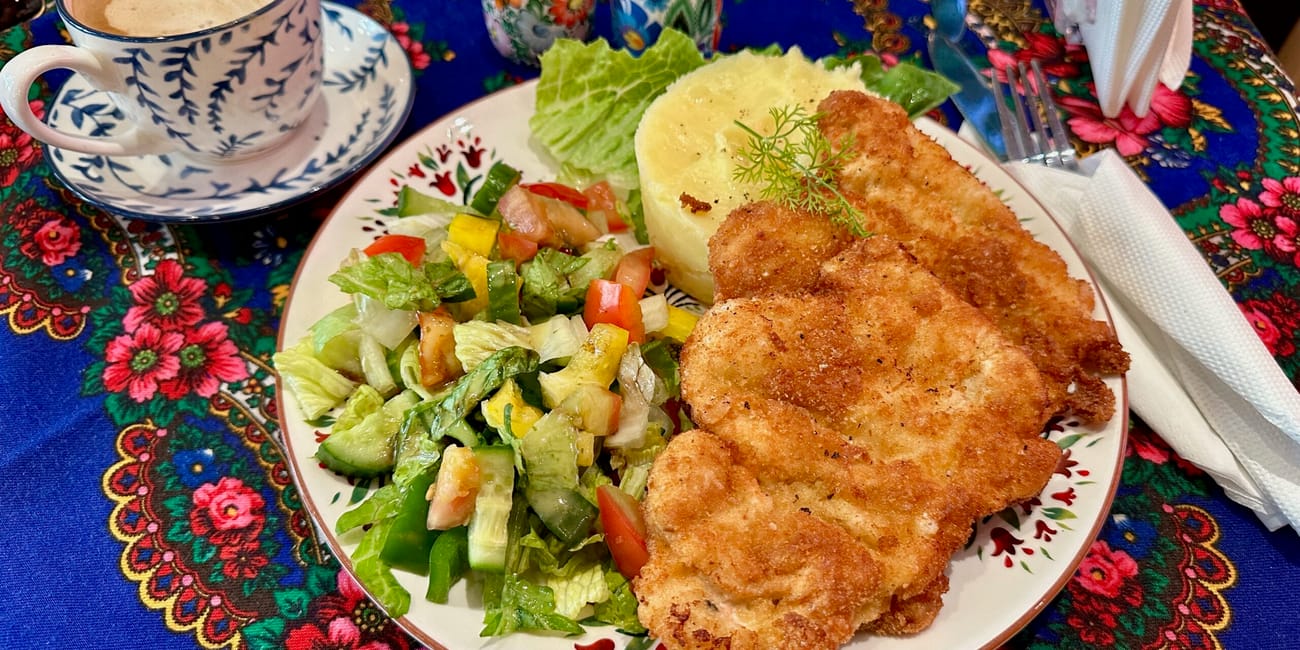Polka restaurant w doha: talerz z kotletem, puree i sałatką oraz filiżanka kawy na kwiecistym obrusie