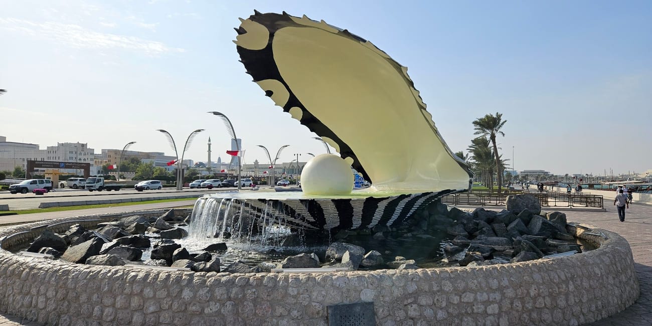 Pomnik doha pearl w dosze z dużą muszlą i fontanną w otoczeniu promenady.