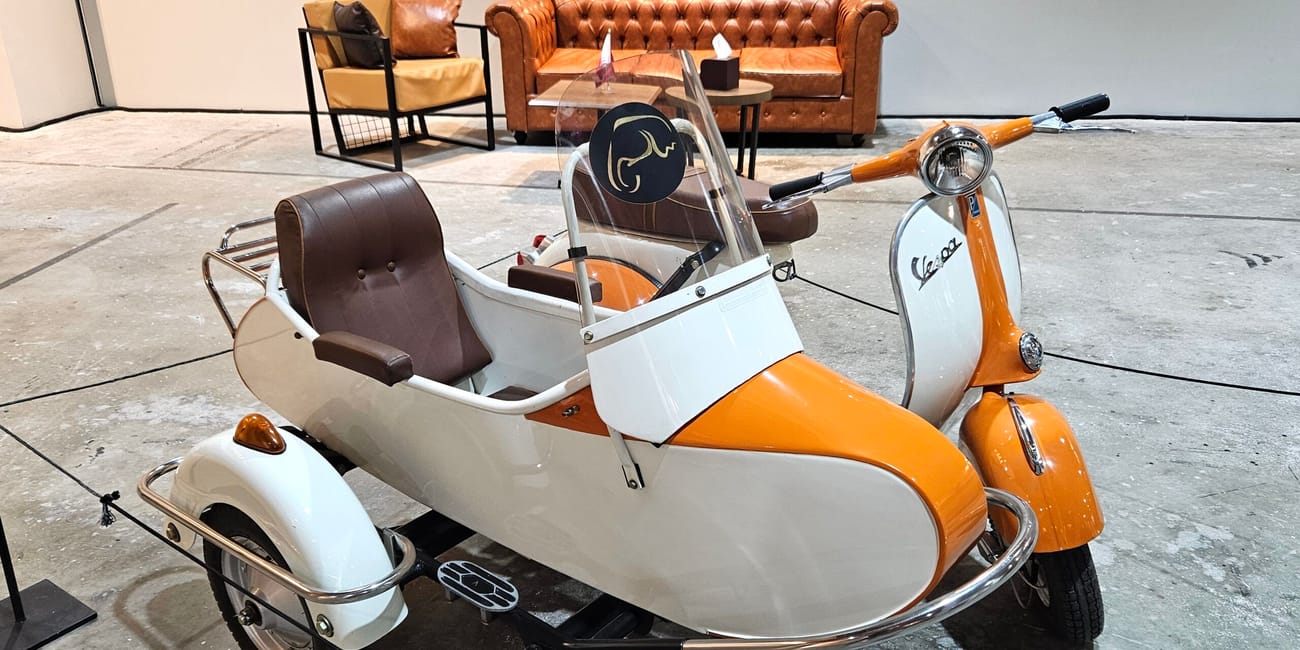 Trójkołowy skuter vespa w doha mawater warehouse, przed skórzaną kanapą i fotelem w tle