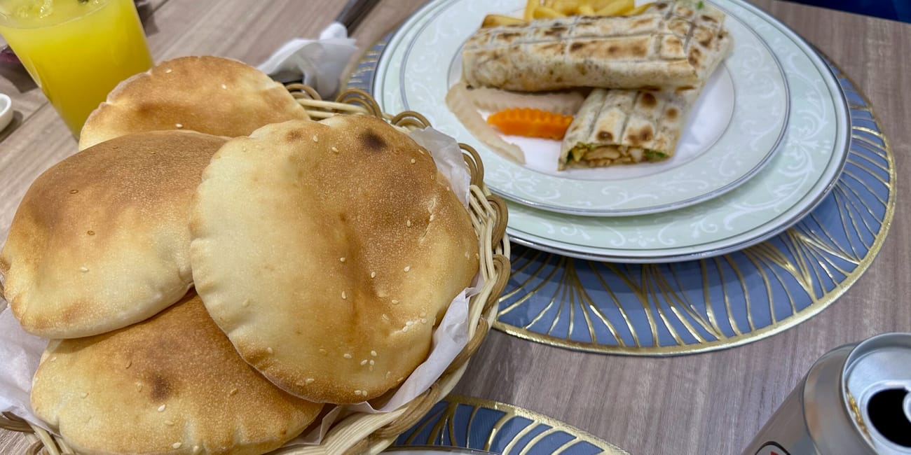 Posiłek w doha foods w katarze: pieczywo, wrapy i napój na stole.