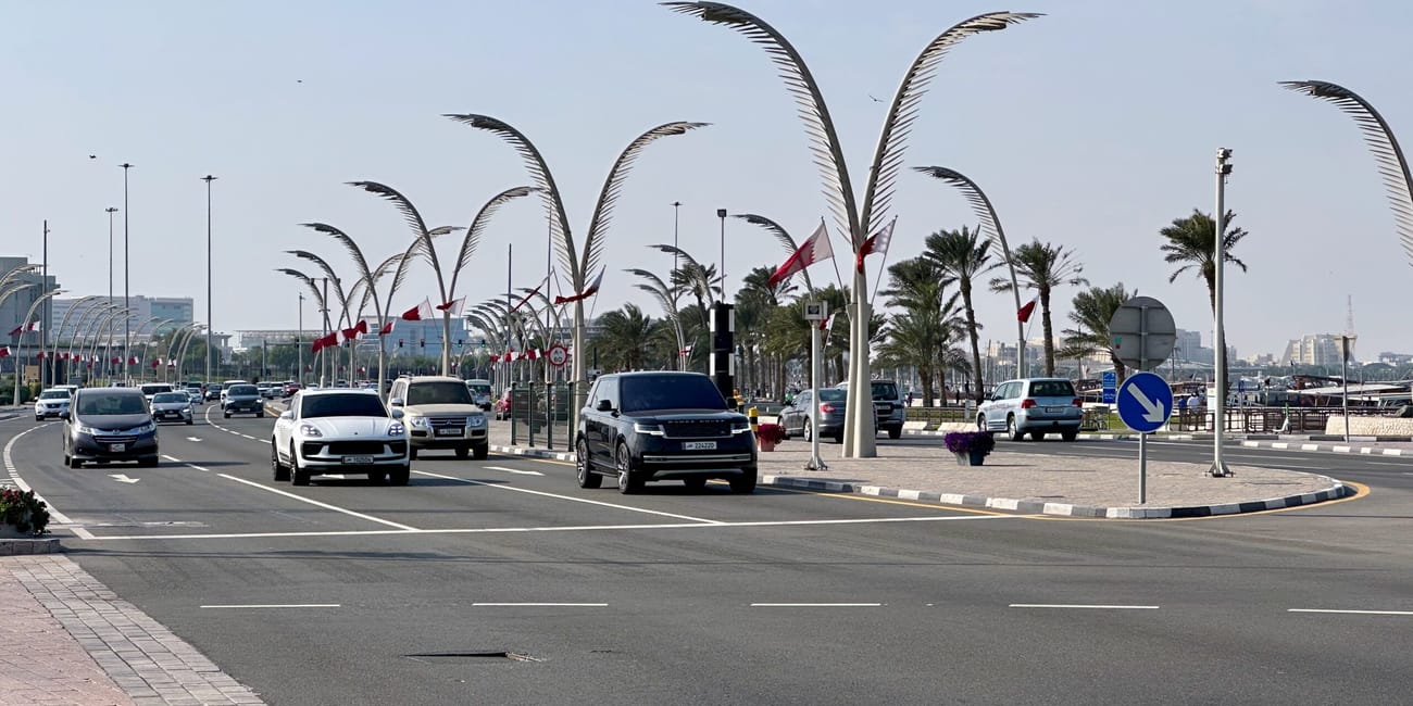 Ruch na promenadzie w doha, katar, z palmami, flagami i samochodami na szerokiej drodze