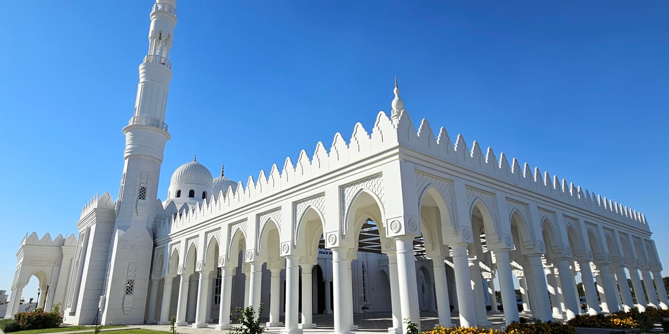 Meczet al sayedah khadeeja w abu zabi z białym minaretem i arkadami pod błękitnym niebem