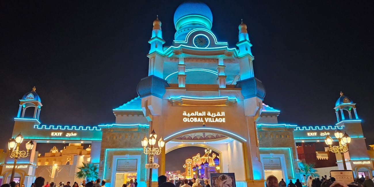 Wejście do global village w dubaju nocą, podświetlone na niebiesko, z tłumem ludzi.