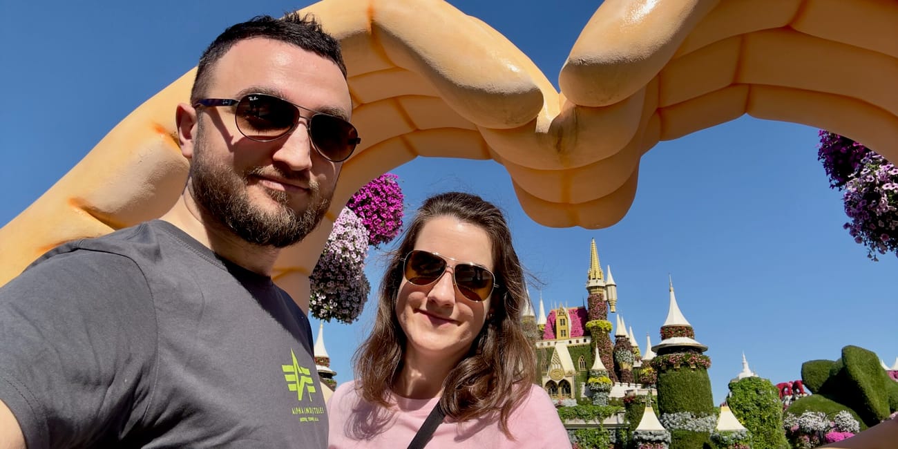 Para w dubai miracle garden pozująca przy kwiatowych dekoracjach i rękach tworzących ramę.