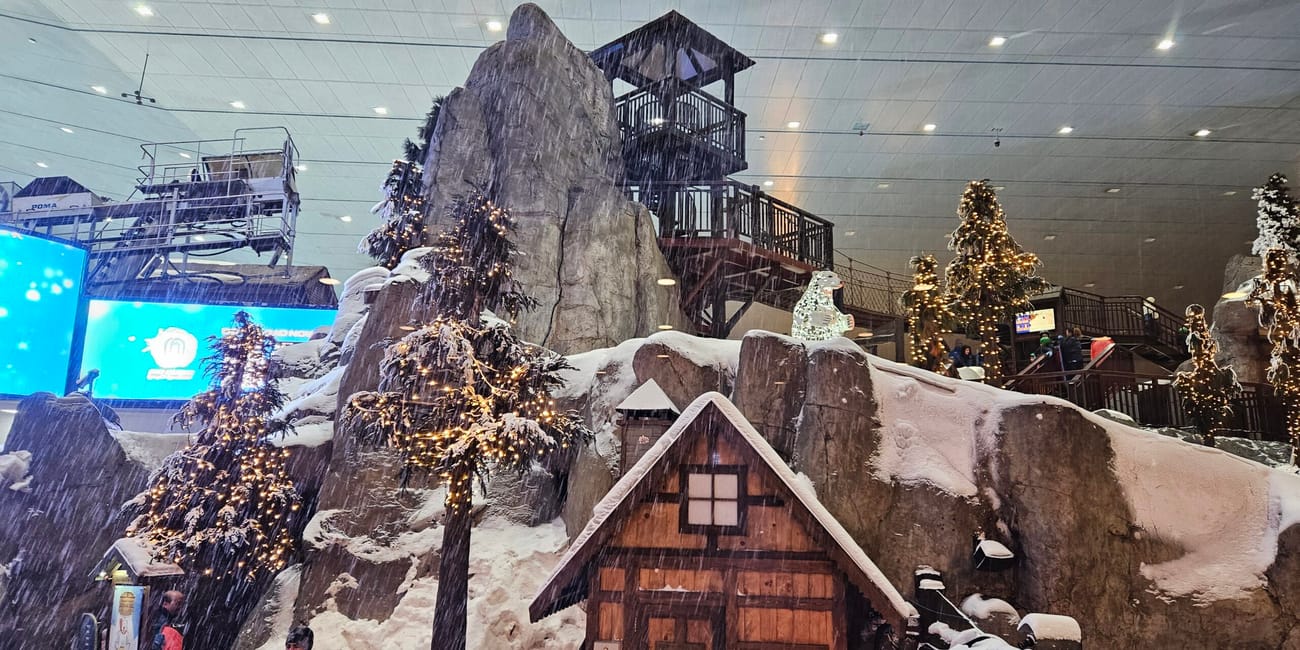 Dubai ski w dubaju: zimowa sceneria z domkiem, skałami i sztucznym śniegiem.
