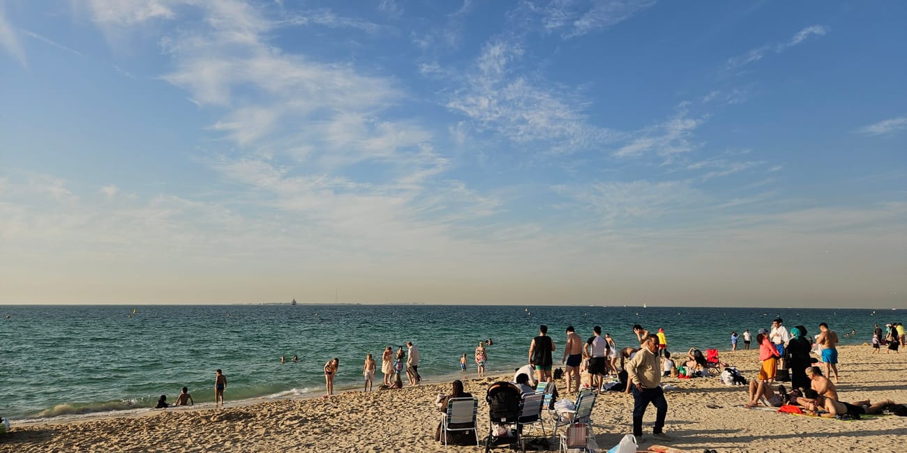 Plaża kite beach w dubaju z plażowiczami, leżakami i spokojnym morzem под błękitnym niebem