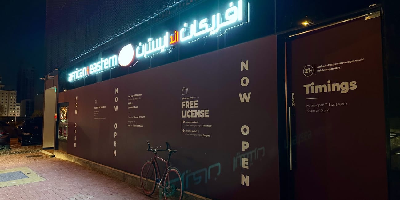 Sklep z alkoholem african eastern w dubaju nocą, z podświetlonym szyldem i rowerem przy wejściu