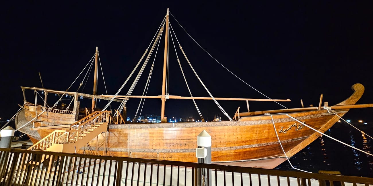 Drewniana łódź dhow przy promenadzie sharjah corniche nocą.