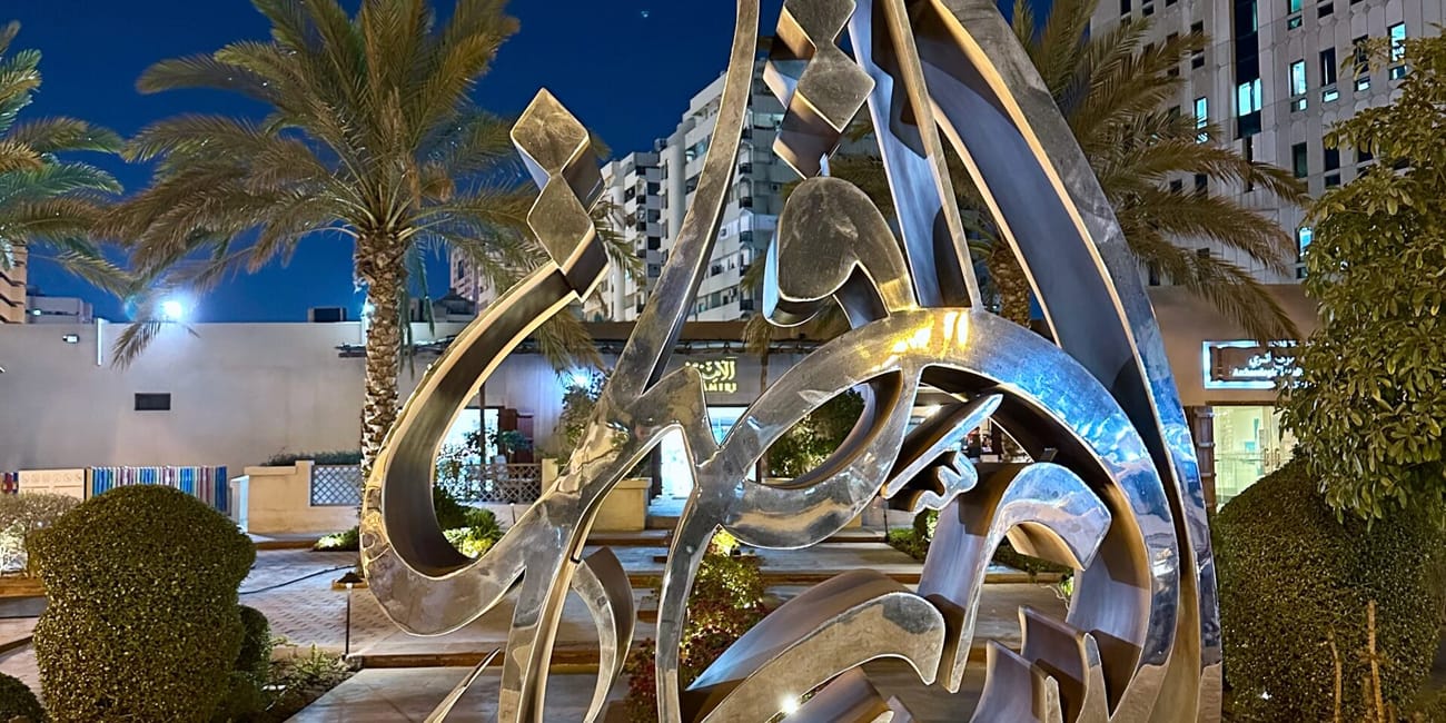 Sharjah corniche w nocy z podświetloną metalową rzeźbą arabskiej kaligrafii.