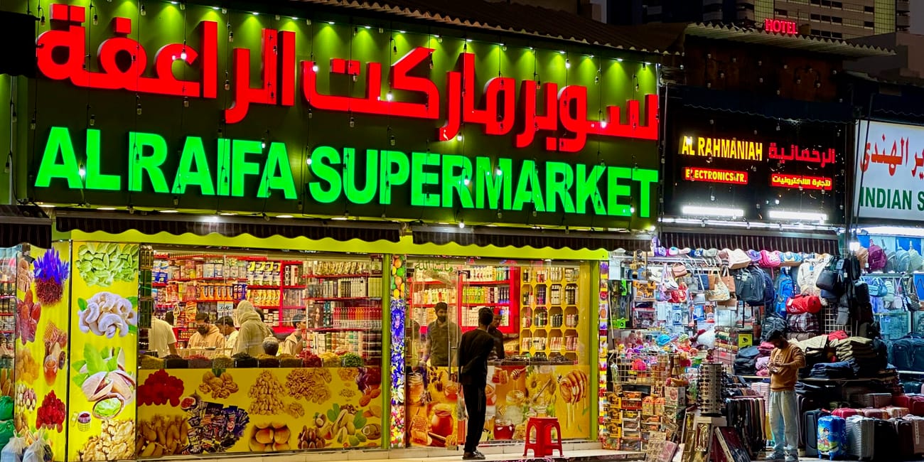 Wieczorny widok na sklep al raifa supermarket w sharjah al ghuwair market, z jaskrawymi szyldami i straganami.
