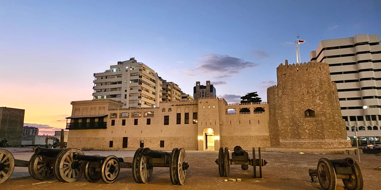Sharjah fort o zmierzchu, z zabytkowymi armatami na placu przed murami