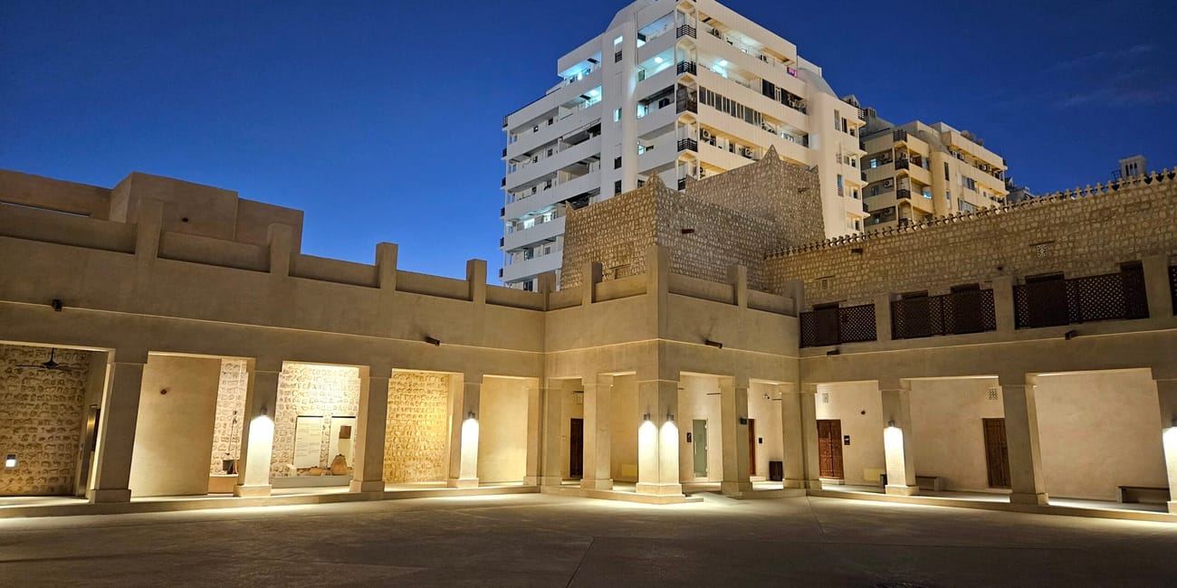 Sharjah fort oświetlony nocą, z historycznymi murami i nowoczesnymi budynkami w tle