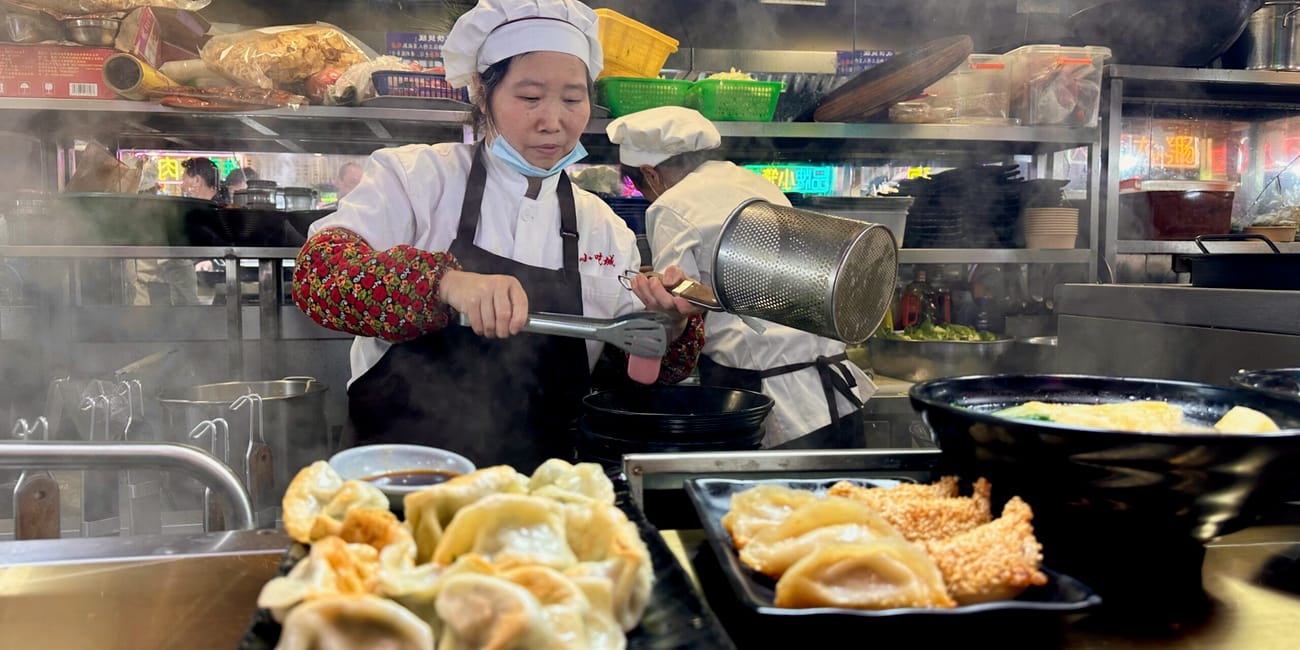 Kucharze przygotowują pierożki i dania w parującej kuchni w szanghaju.