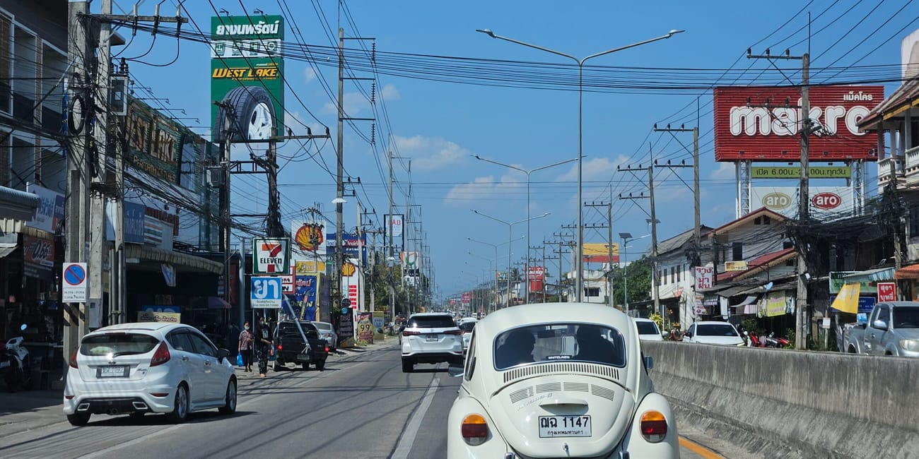 Ulica w chiang mai z białym volkswagenem garbusem na drodze i gęstą siecią kabli nad jezdnią