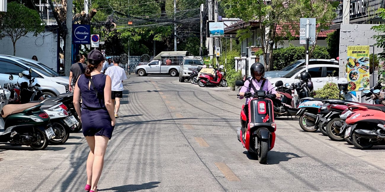 Ulica w chiang mai z pieszymi, skuterami i zaparkowanymi motocyklami w słoneczny dzień