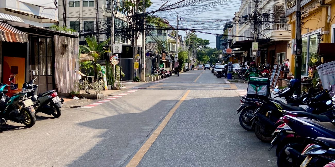 Ulica w chiang mai z zaparkowanymi skuterami i gęstą plątaniną przewodów nad jezdnią.