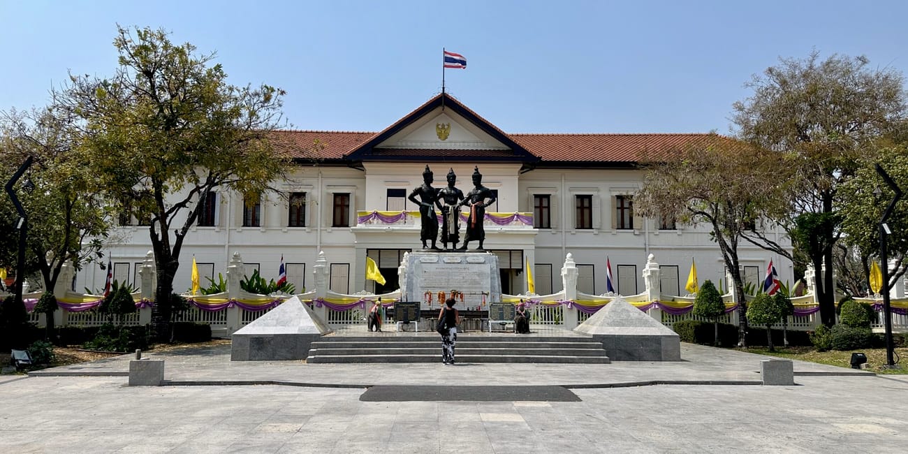 Chiang mai city arts z pomnikiem trzech postaci przed białym budynkiem i flagą tajlandii