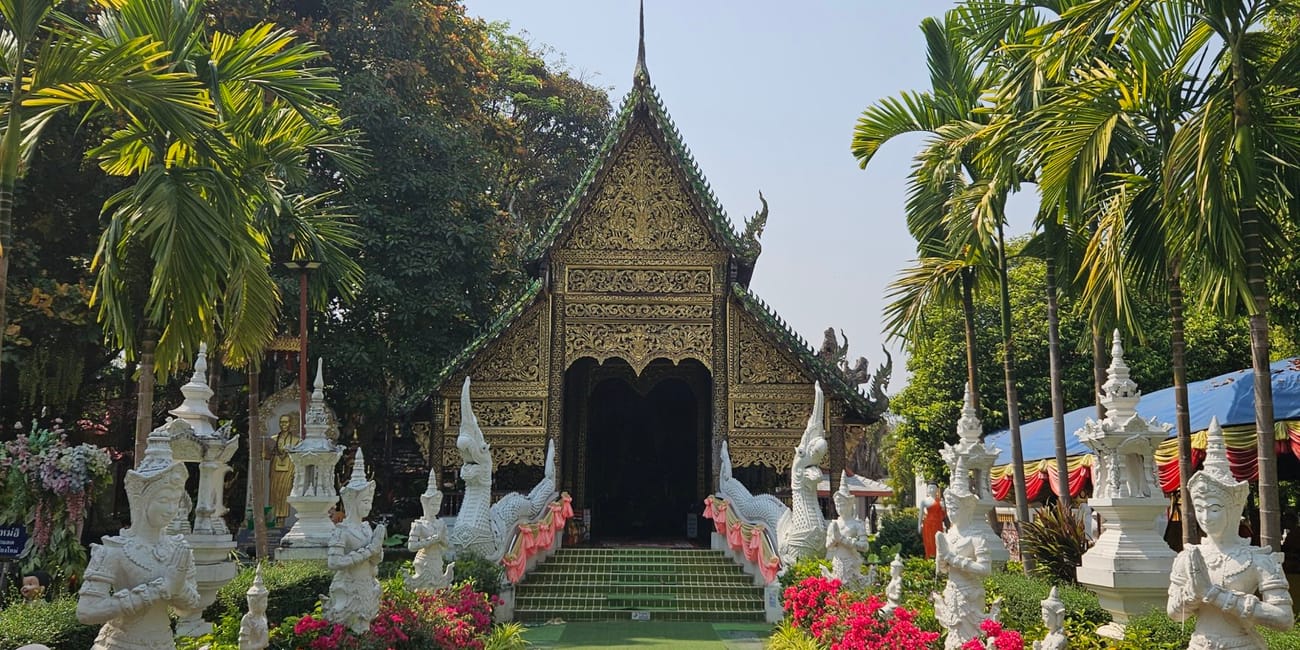 Świątynia wat tha mai w chiang mai, z ozdobnym wejściem, palmami i kwiatami