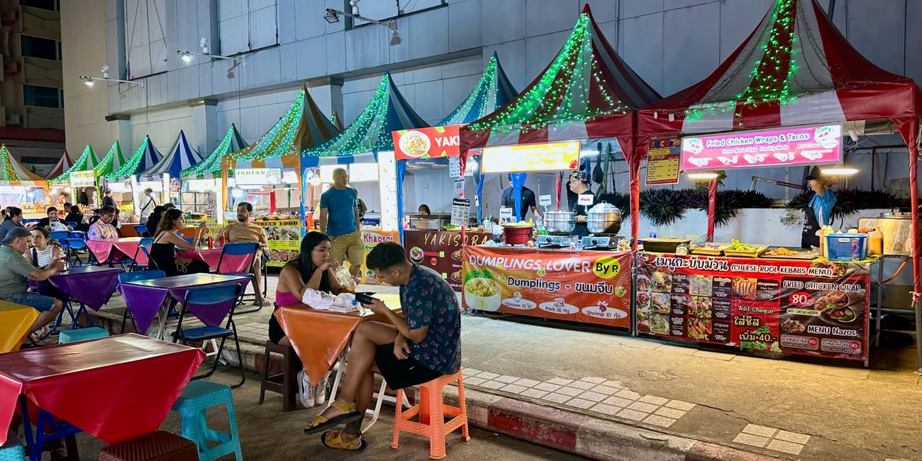 Stoiska z jedzeniem i stoliki w chiang mai night bazaar wieczorem, z kolorowymi namiotami i neonowymi szyldami.