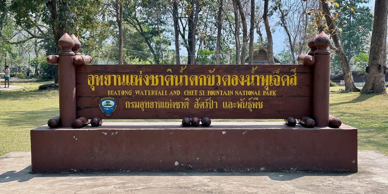 Tablica buatong waterfall and chet si fountain national park w chiang mai, otoczona drzewami.