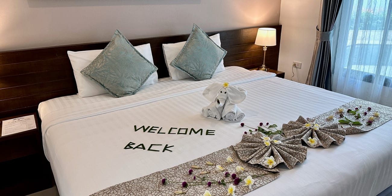 Pokój hotelowy w phuket z udekorowanym łóżkiem „welcome back” i ręcznikowym słoniem.