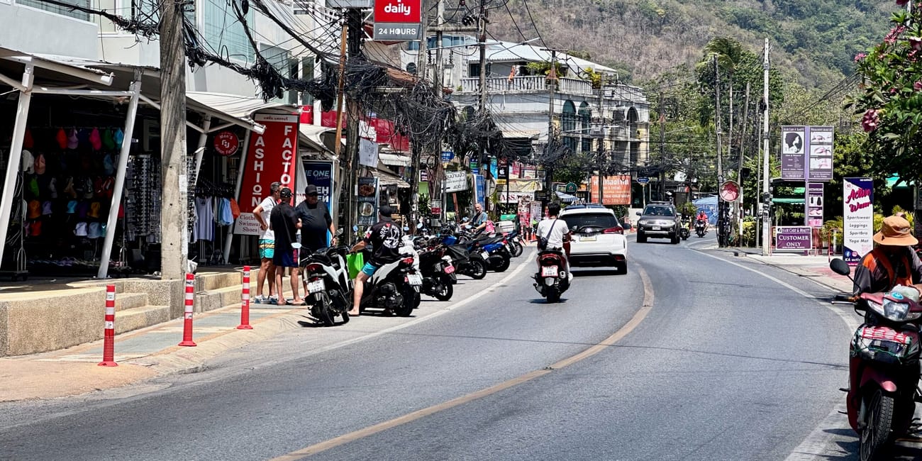 Ulica w phuket z ruchem skuterów, sklepami i górą w tle