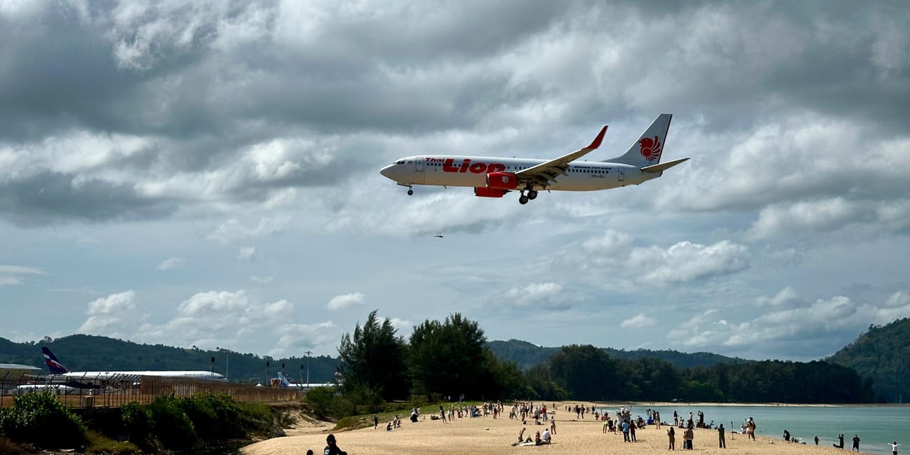 Mai khao beach w phuket z nisko lecącym samolotem nad plażą pełną ludzi