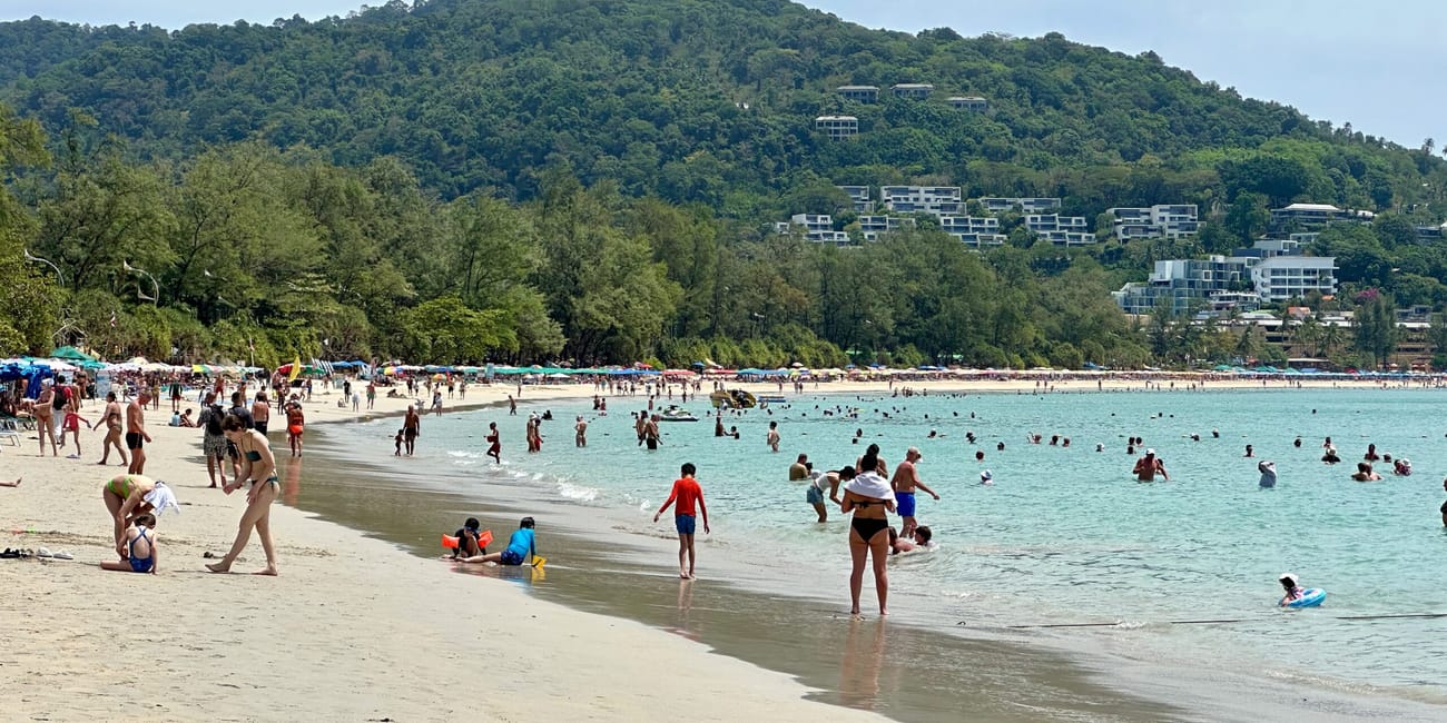 Plaża kata beach w phuket z turystami kąpiącymi się w morzu i zielonym wzgórzem w tle