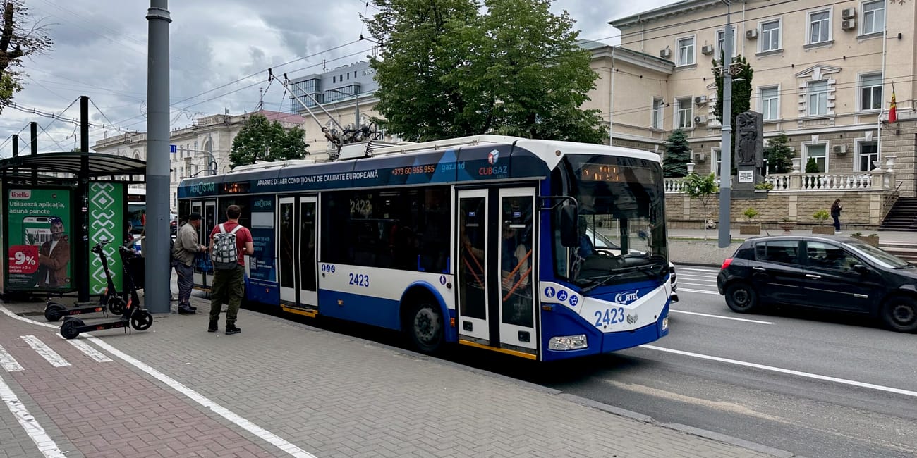 Chisinau public transport bus stopped at a curb in moldova, with trolley wires overhead and pedestrians nearby.