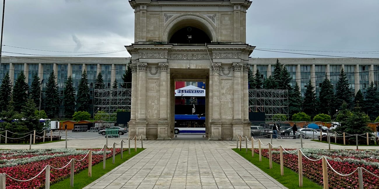 Łuk triumfalny w kiszyniowie na tle pochmurnego nieba, z alejką i rabatami kwiatów na pierwszym planie
