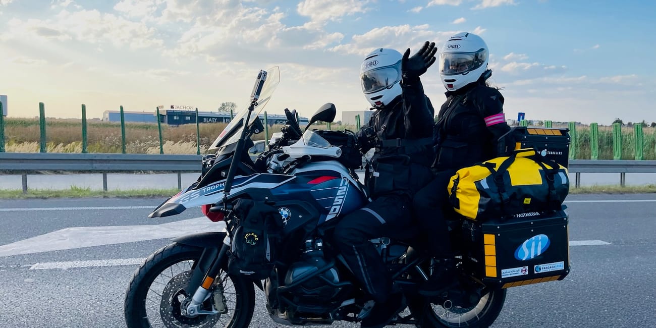 Dwoje motocyklistów na turystycznym motocyklu na trasie w desert horizons, jedno macha do kamery.